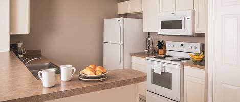 A modern kitchen with white appliances, a sink, and a countertop with croissants and coffee cups.