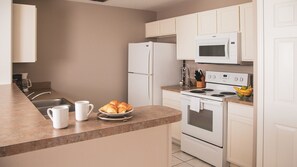 A modern kitchen with white appliances, a sink, and a countertop with croissants and coffee cups.