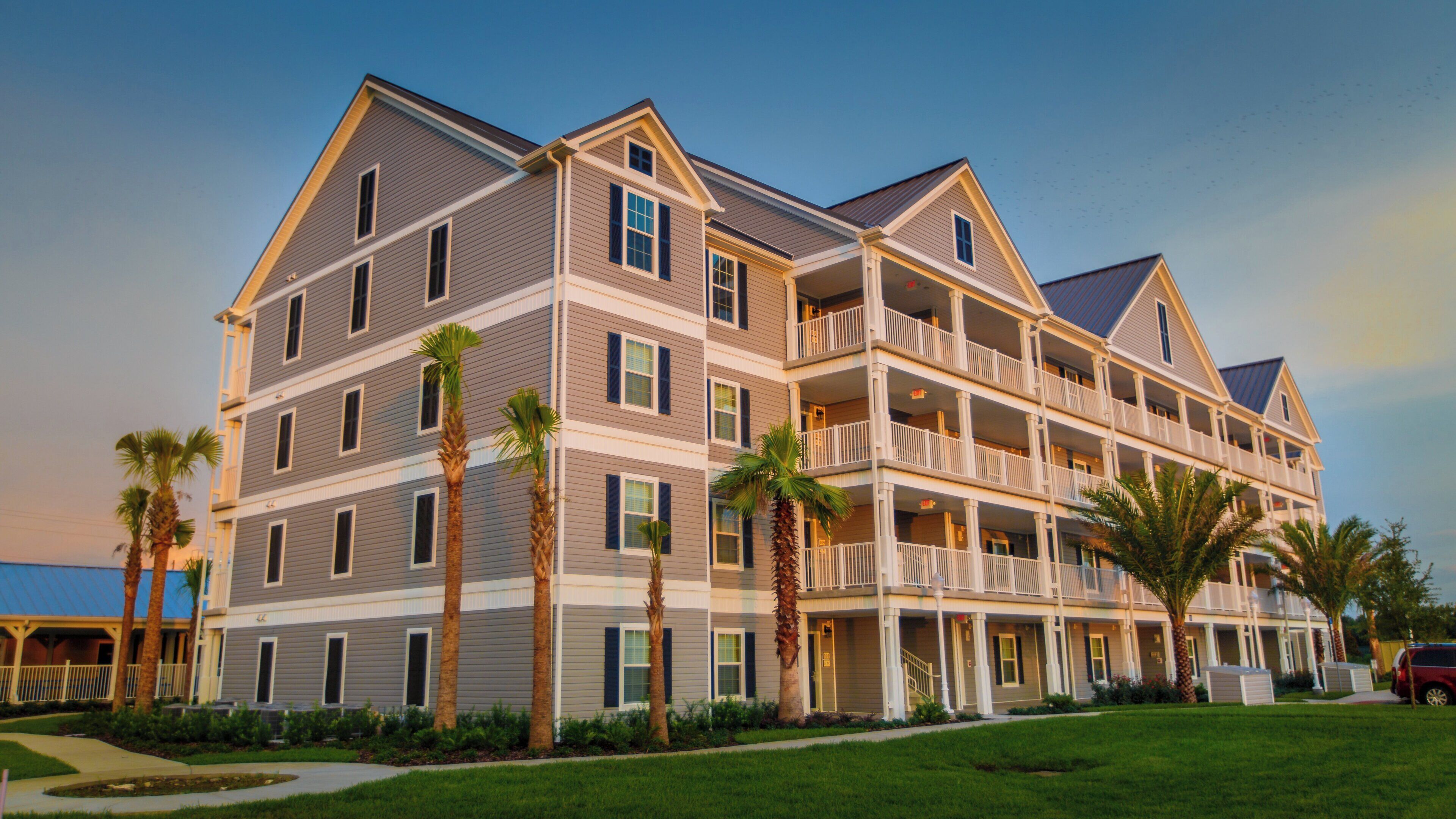 A multi-story hotel with balconies, palm trees, and a view of the ocean.