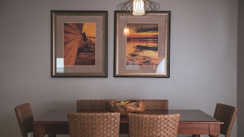 A dining area with a wooden table and wicker chairs, framed artwork on the wall, and a woven basket on the table.