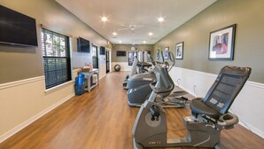 Un gimnasio con equipo de ejercicio, un ventilador de techo y un reloj en la pared.