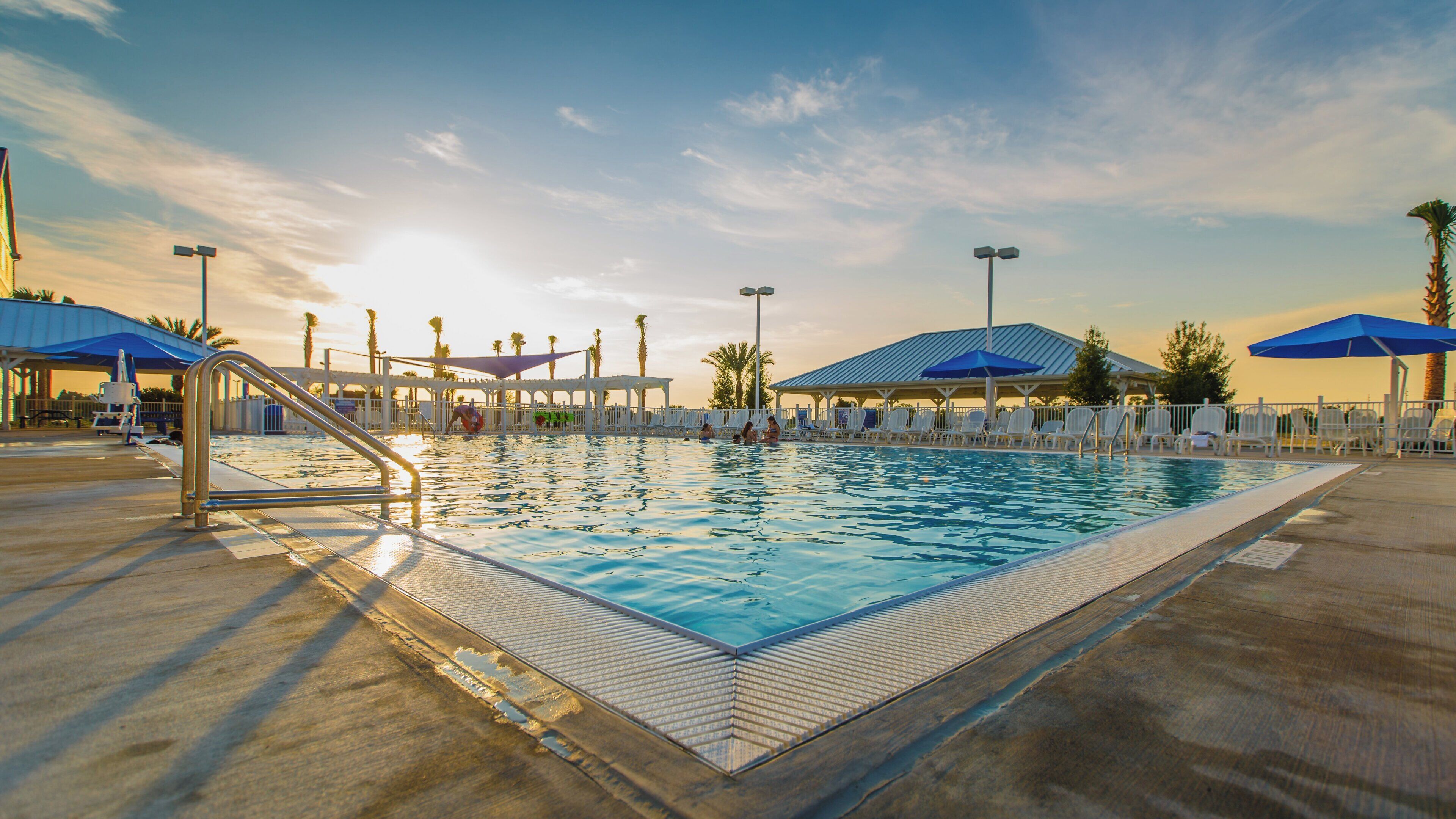 Une piscine avec une terrasse ensoleillée, des chaises longues et des parasols.