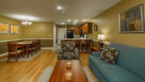 A living room with a blue sofa, wooden coffee table, and patterned armchair. There is a dining area with wooden chairs and a table, and a kitchen with wooden cabinets and a refrigerator. - Holiday Inn Club Vacations Orlando Breeze Resort by IHG (Davenport)
