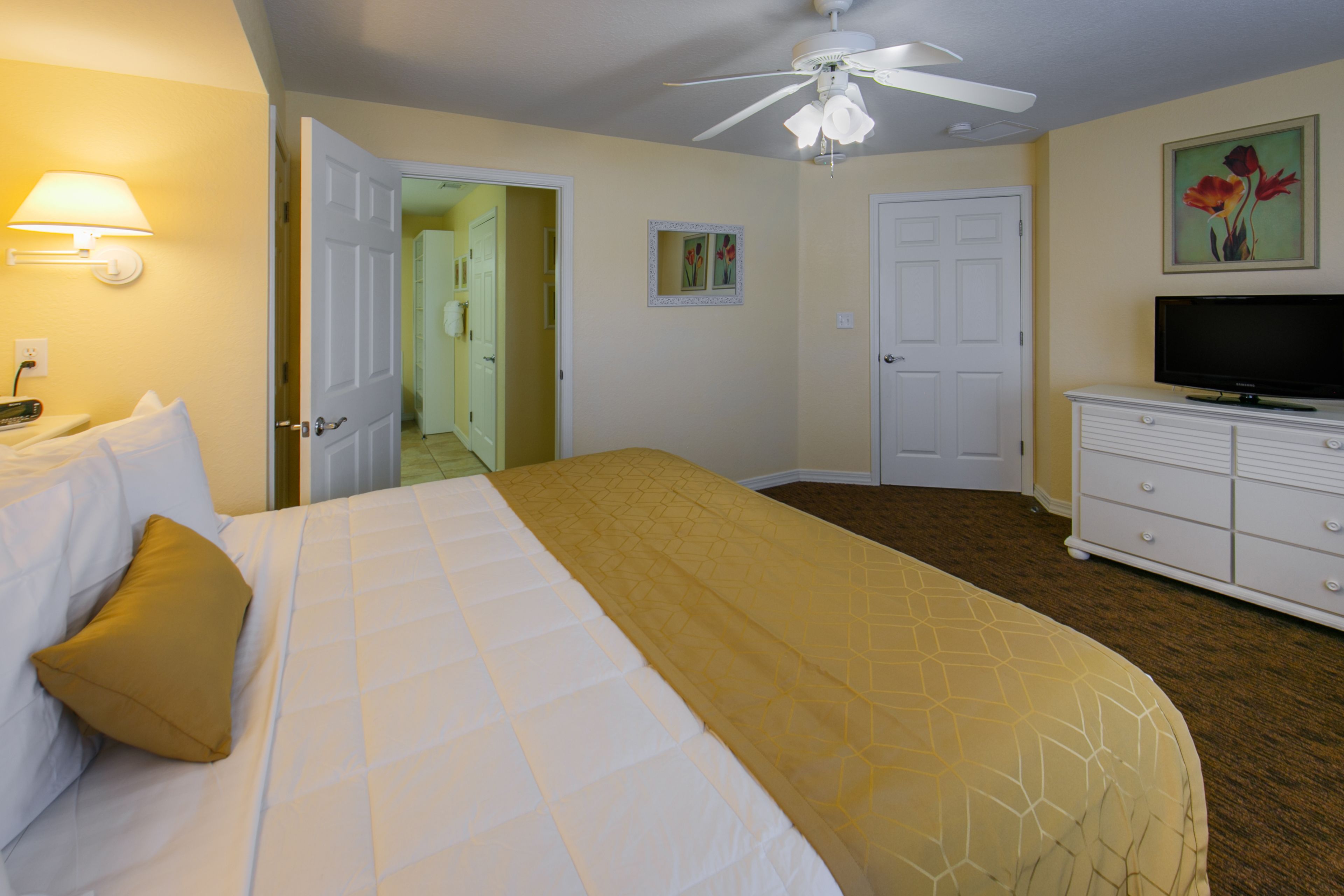 A hotel room with a bed, a television, a dresser, and a ceiling fan.