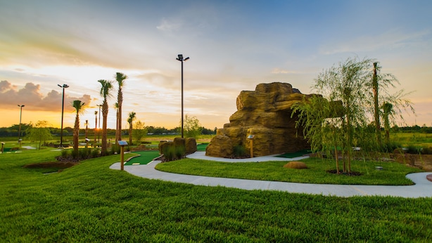 A golf course with a large rock formation, palm trees, and a well-maintained green.