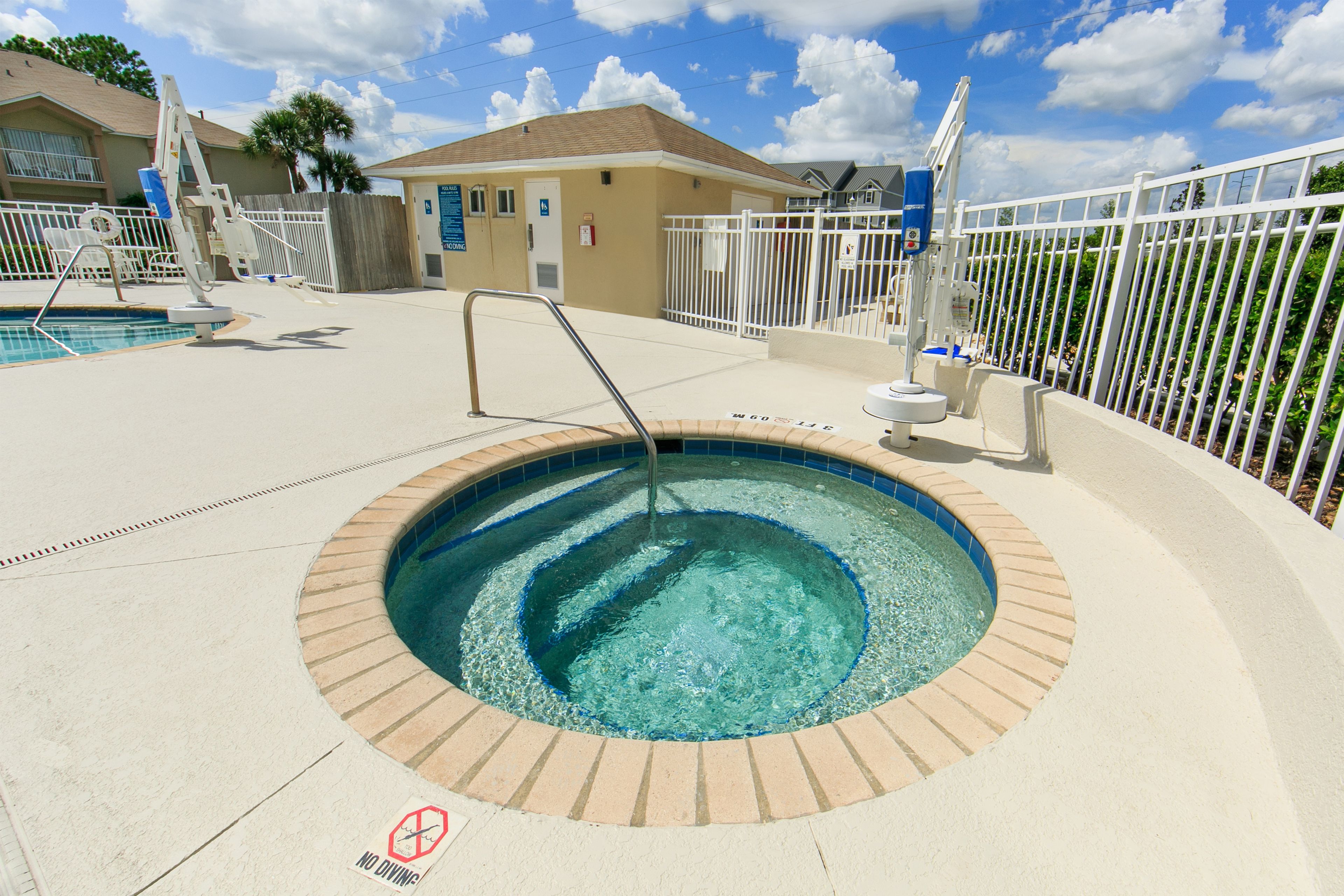 Ein Whirlpool mit Pool, umgeben von einem weißen Zaun, mit blauem Himmel im Hintergrund.