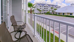 A balcony with two chairs, a view of a parking lot, and a building with multiple balconies and palm trees. - Holiday Inn Club Vacations Orlando Breeze Resort by IHG (Davenport)