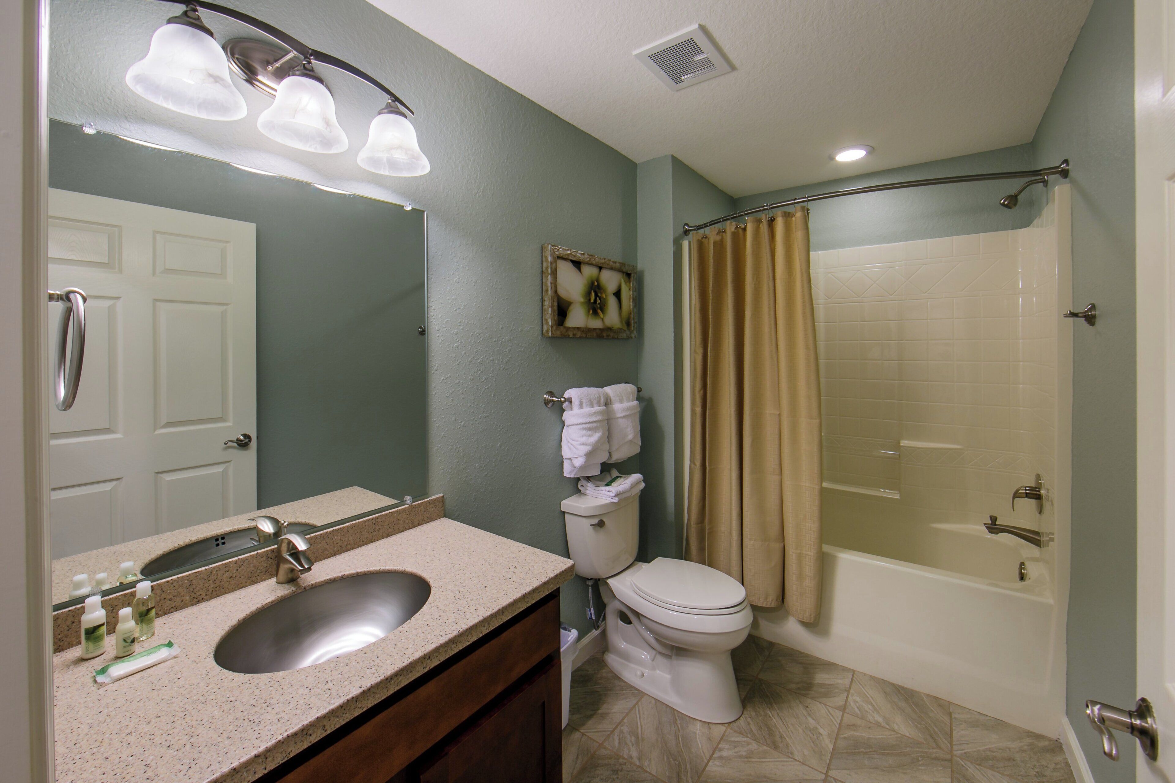 A bathroom with a sink, toilet, shower, and a mirror.