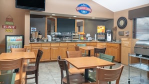 A breakfast area with wooden tables and chairs, a coffee station, and a television mounted on the wall. - Baymont by Wyndham Lakeville (Lakeville)