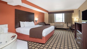 A hotel room with a large bed, a desk, a chair, a TV, and a window with curtains. - Baymont by Wyndham Lakeville (Lakeville)