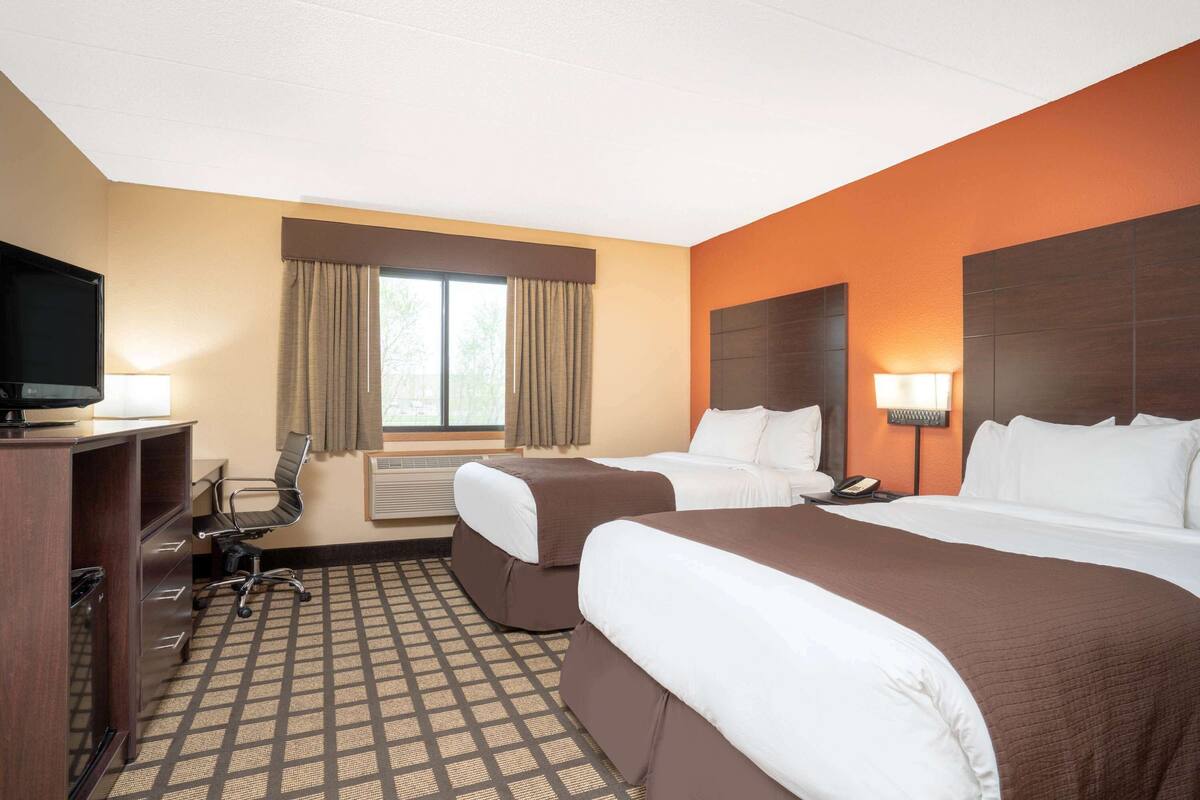 A hotel room with two beds, a desk with a TV, a chair, and a window with curtains.