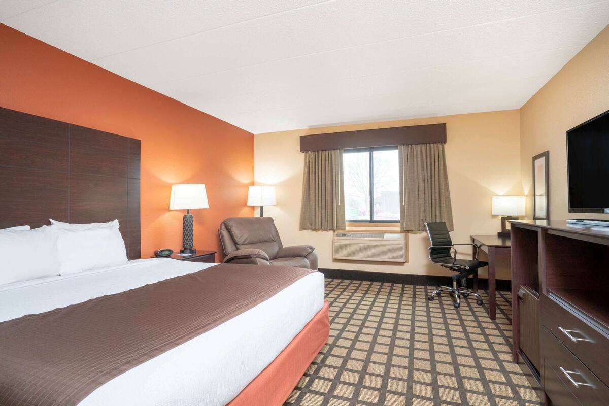 A hotel room with a large bed, two chairs, a desk, and a TV.