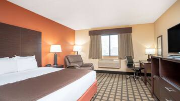 A hotel room with a large bed, two chairs, a desk, and a TV.