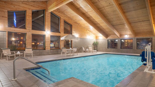 A swimming pool with tiled flooring, wooden ceiling beams, and multiple windows. - Baymont by Wyndham Lakeville (Lakeville)