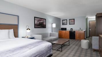 A hotel room with a bed, a sofa, a coffee table, a desk, a kitchenette, and a bathroom.