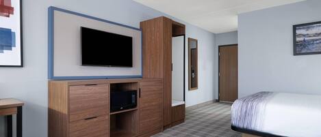 A hotel room with a bed, a television, a wooden cabinet, and a door.