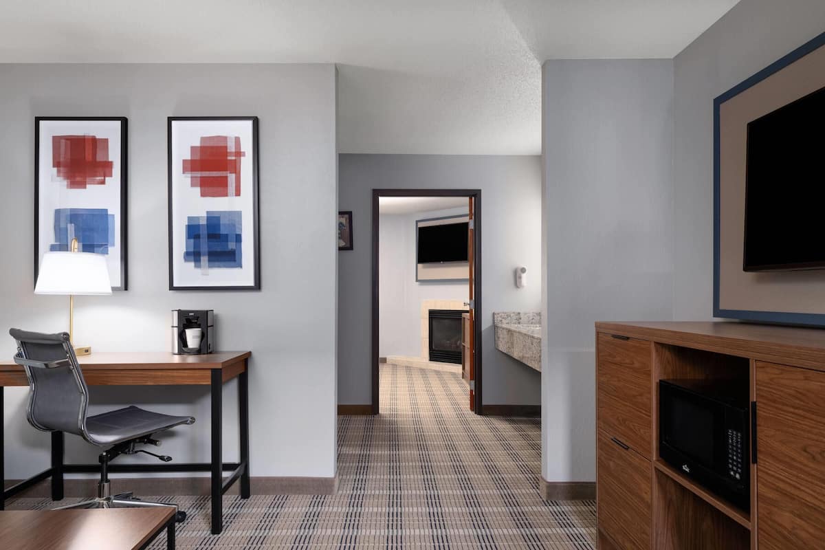 A hotel room with a desk, chair, coffee machine, television, and a microwave.