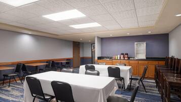A conference room with tables, chairs, a kitchenette, and a blue carpeted floor.
