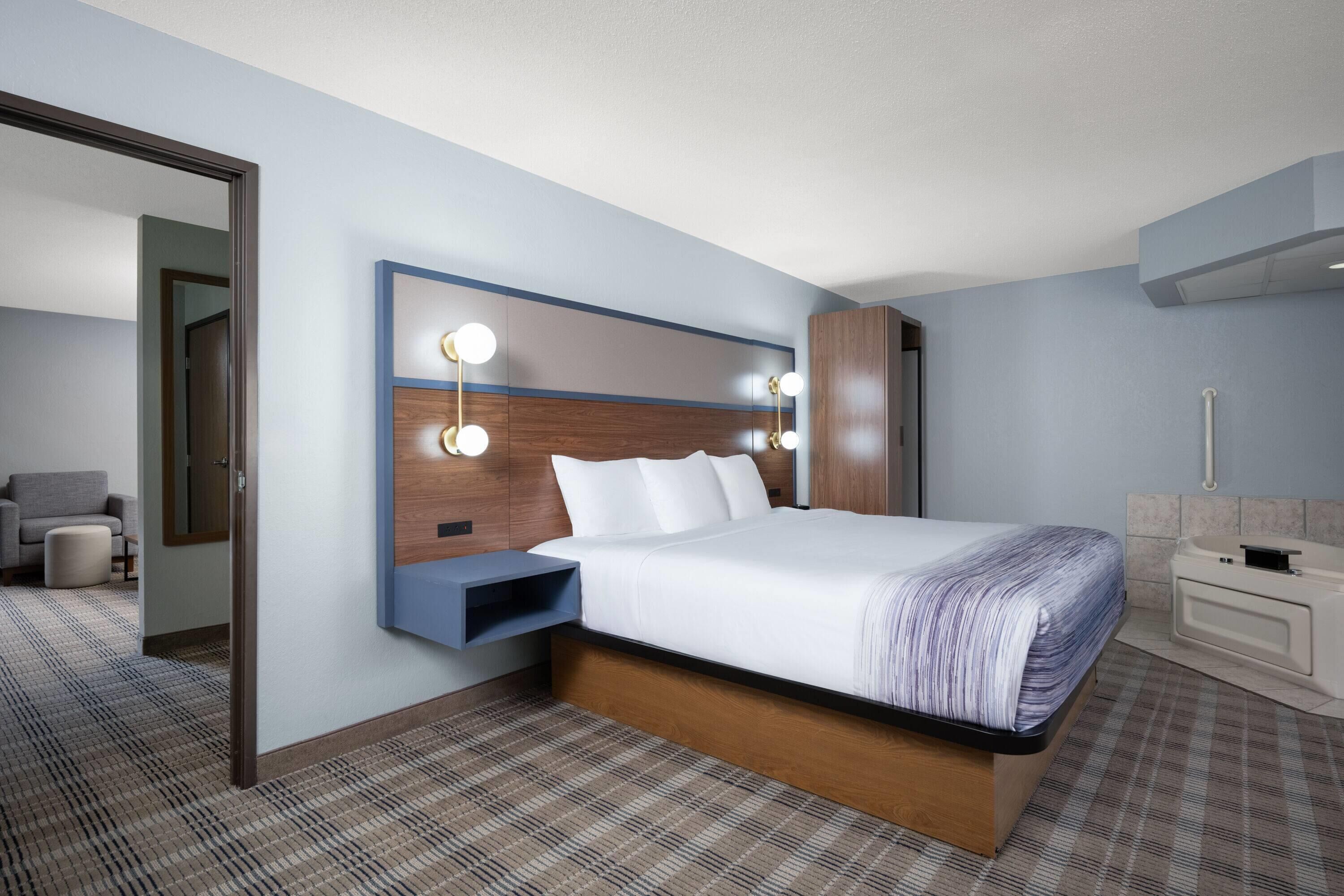 A hotel room with a bed, bedside table, wall-mounted lights, a mirror, and a bathroom with a sink and toilet.