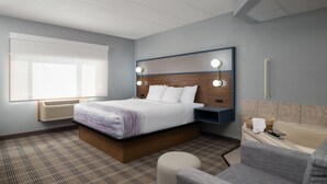 Una camera d'albergo con un letto, un comodino, una lampada e un bagno con una vasca e un lavandino.