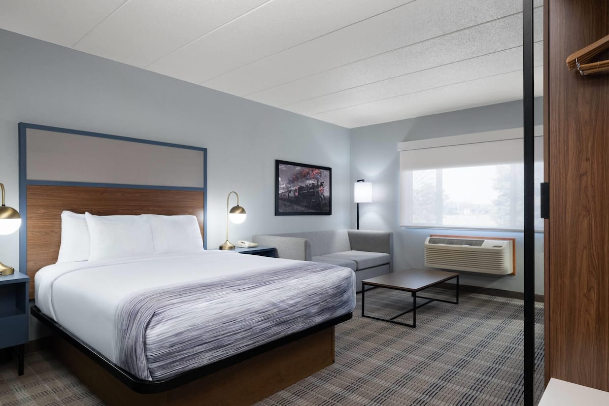 A hotel room with a bed, bedside tables, a sofa, a coffee table, a wall-mounted air conditioner, and a window with a view.