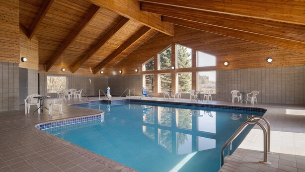 Una piscina coperta con travi in legno, pareti piastrellate e sedie in plastica bianca.