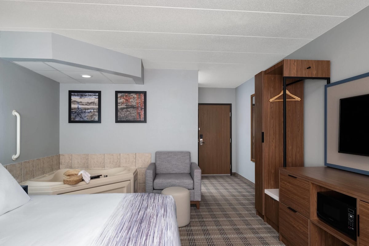 A hotel room with a bed, a sofa, a chair, a TV, a wooden cabinet, and a door.
