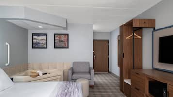 Ein Hotelzimmer mit einem Bett, einem Sofa, einem Sessel, einem Fernseher, einem Holzschrank und einer Tür.