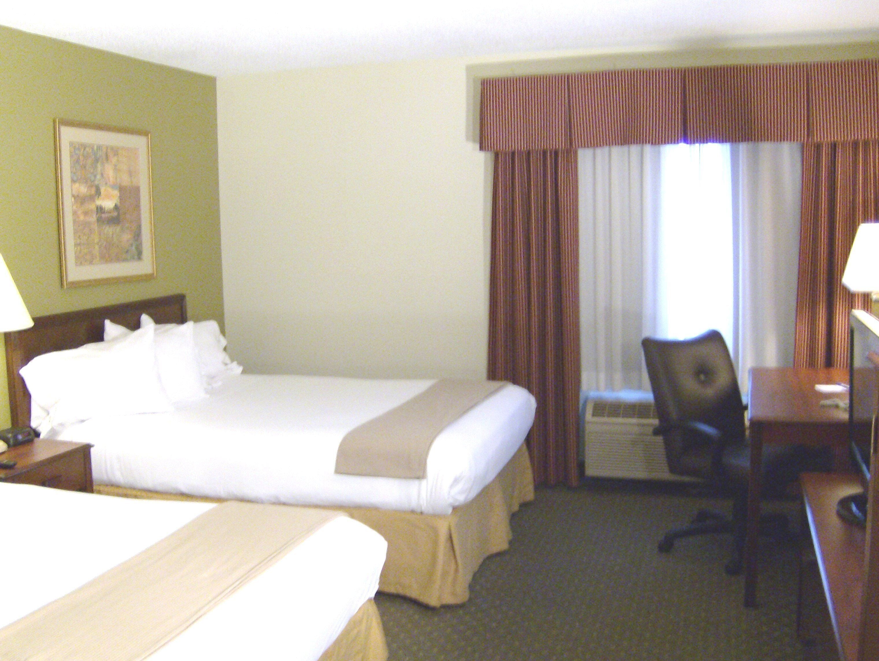 Een hotelkamer met een bed, bureau, stoel en raam met gordijnen.