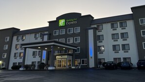 Edificio de Holiday Inn Express con entrada cubierta, varias ventanas y un estacionamiento con automóviles.