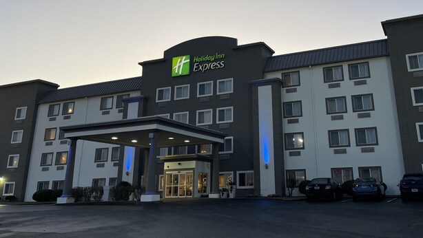 Edificio de Holiday Inn Express con entrada cubierta, varias ventanas y un estacionamiento con automóviles.