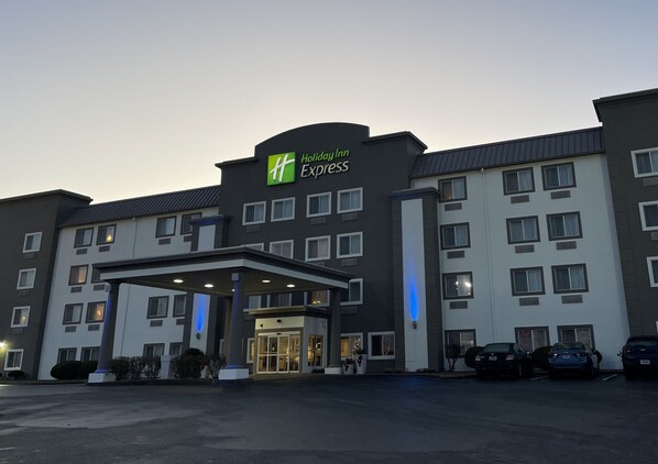 Edificio de Holiday Inn Express con entrada cubierta, varias ventanas y un estacionamiento con automóviles.