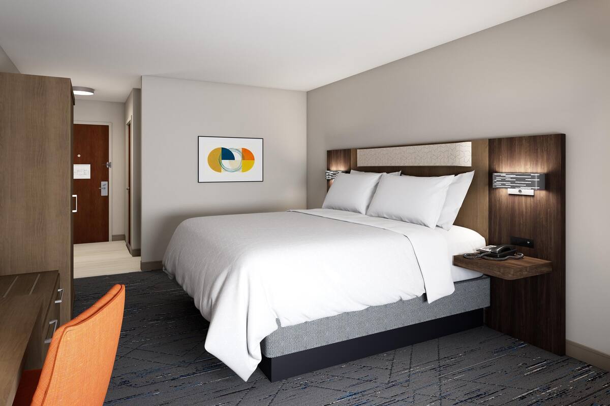 Una habitación de hotel moderna con una cama grande, un escritorio y una mesita de noche.