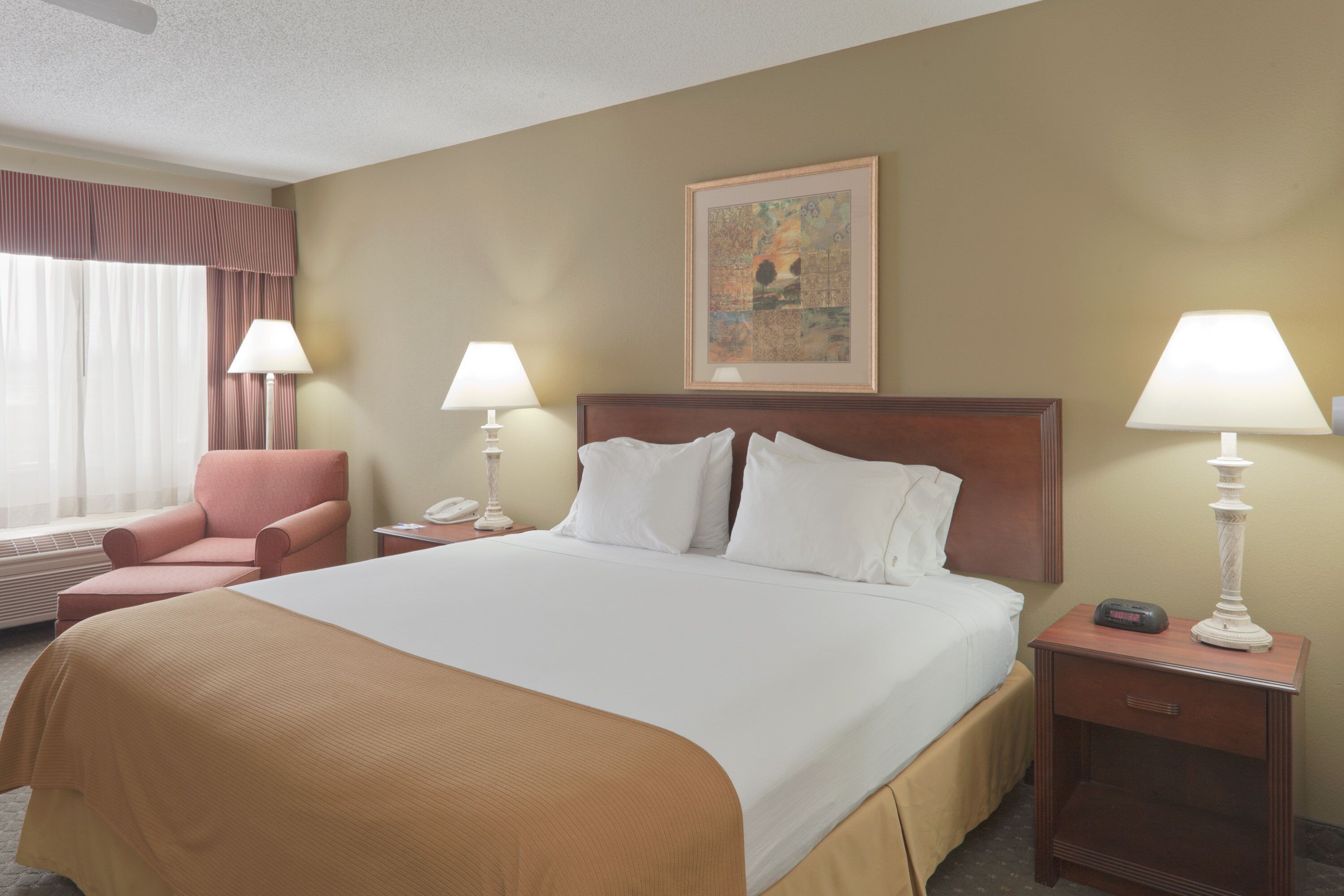A hotel room with a large bed, two bedside lamps, a chair, a painting on the wall, and a telephone on the nightstand.