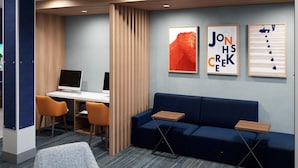 Un espacio de oficina moderno con un escritorio, dos sillas, un sofá azul y tres obras de arte enmarcadas en la pared.