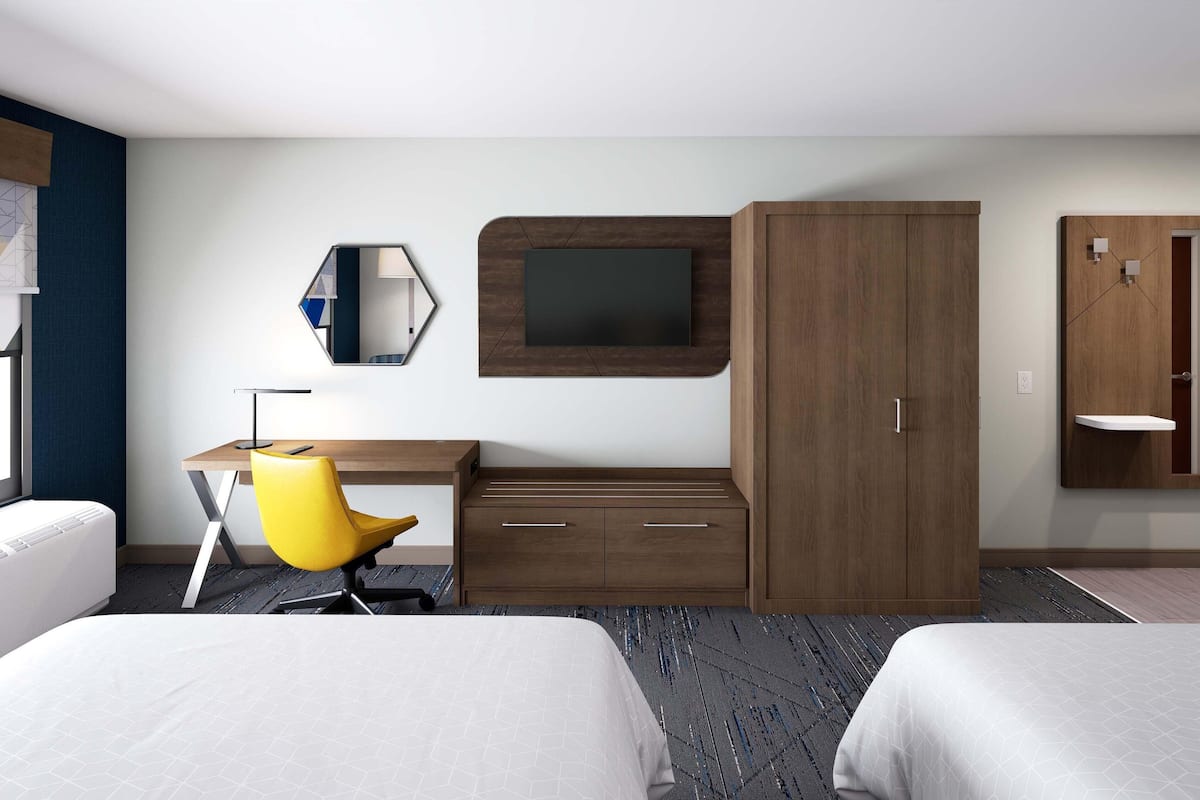 Una habitación de hotel con dos camas, un escritorio con silla, televisión y armario.