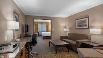 A hotel room with a kitchenette, a bed, a sofa, a coffee table, and a TV.