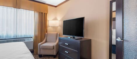 Une chambre d’hôtel avec un lit, un téléviseur posé sur une commode, une chaise et une lampe.