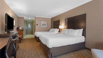A hotel room with two beds, a desk, a television, and a patterned carpet.