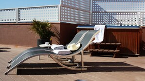 A sun loung Chair with a towel and a bottle on a deck. - Hotel Garbi Millenni (Barcelona)