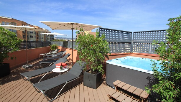 A rooftop patio with lounge chairs, umbrellas, a hot tub, and potted plants. - Hotel Garbi Millenni (Barcelona)