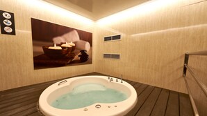 A spa room with a large bathtub, wooden flooring, and a wall-mounted picture of candles. - Hotel Garbi Millenni (Barcelona)