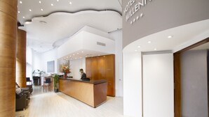 A hotel reception area with a wooden reception desk, a receptionist, and a modern interior design. - Hotel Garbi Millenni (Barcelona)