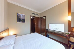 Una habitación de hotel con una cama, televisión, escritorio con lámpara y espejo.