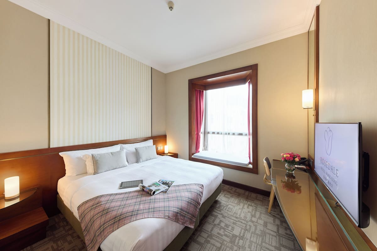 A hotel room with a bed, a desk, a TV, and a window with curtains.