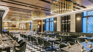 A restaurant with checkered flooring, black and green chairs, and a bar area in the background. - Rosedale Hotel Hong Kong (Hong Kong)