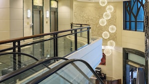 An interior view of a hotel lobby with a glass railing, an escalator, and a decorative light fixture. - Rosedale Hotel Hong Kong (Hong Kong)
