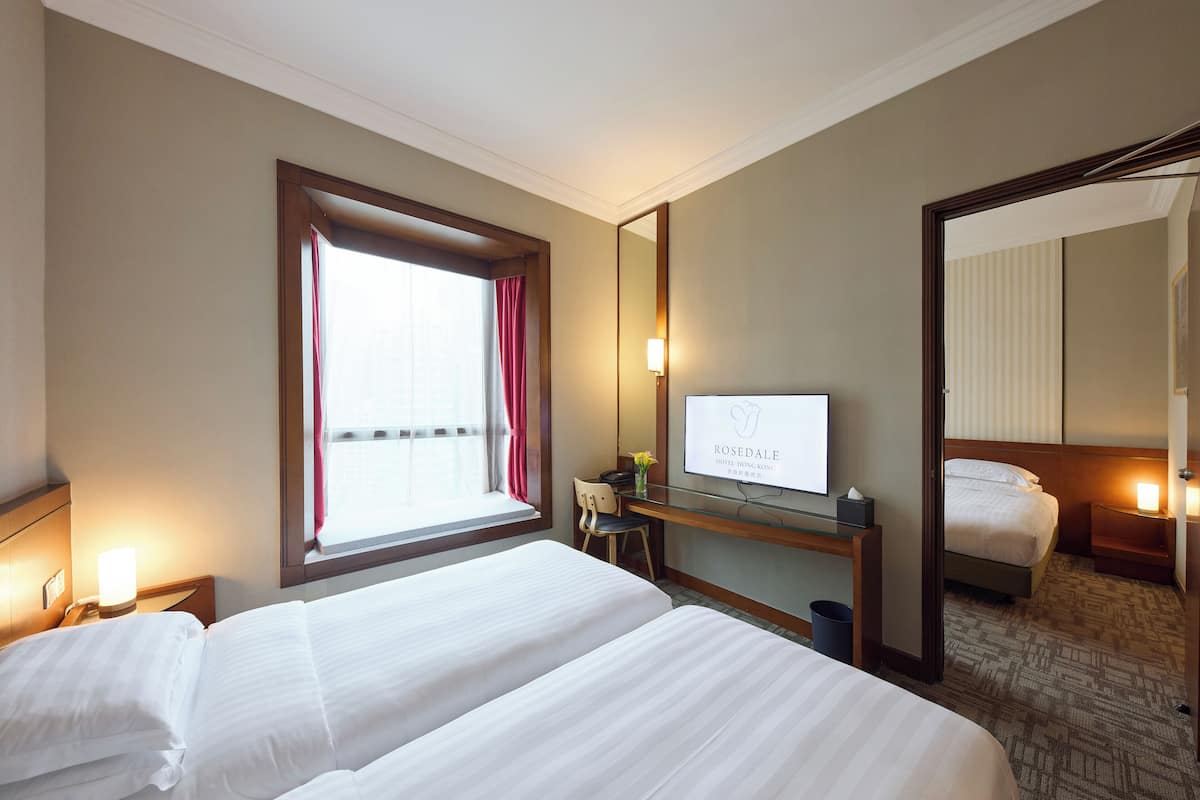 A hotel room with two beds, a desk, a chair, a TV, and a large mirror.