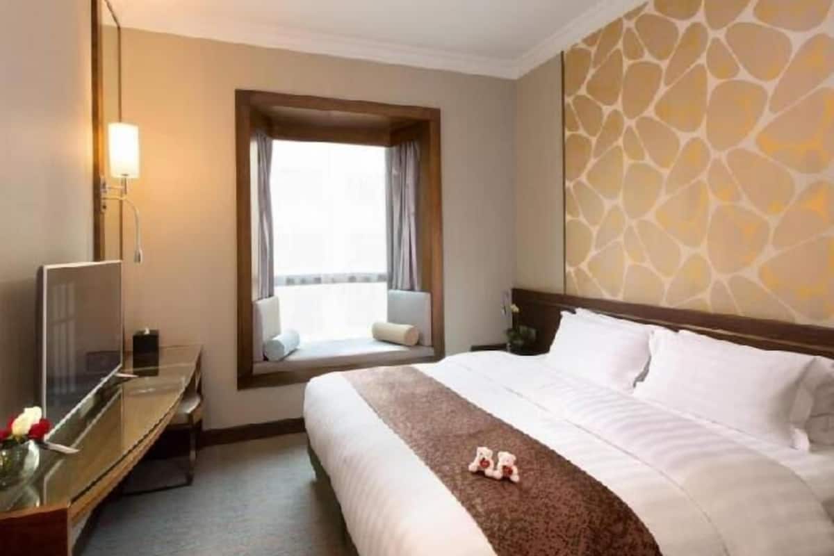 A hotel room with a bed, a desk with a computer, a window with curtains, and a wall with a patterned design.