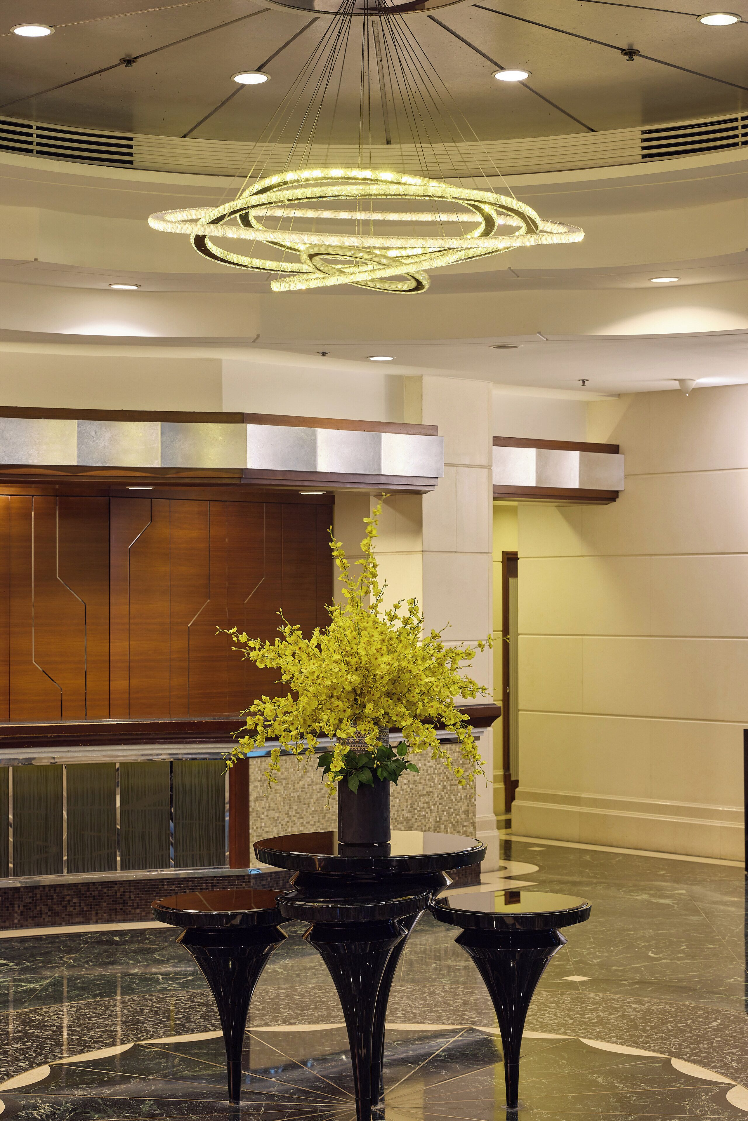 A lobby with a modern chandelier, a reception desk, and a potted plant.